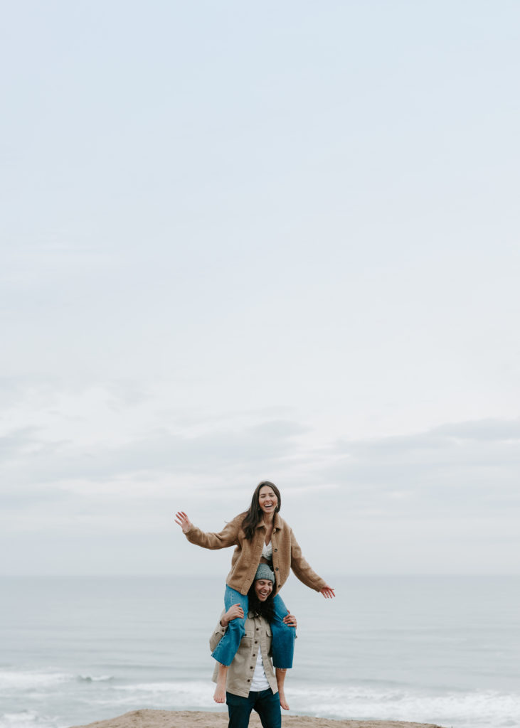 Woman sitting on her partners shoulder as she is flying her arms around and they are both laughing during their California engagement photos in San Francisco