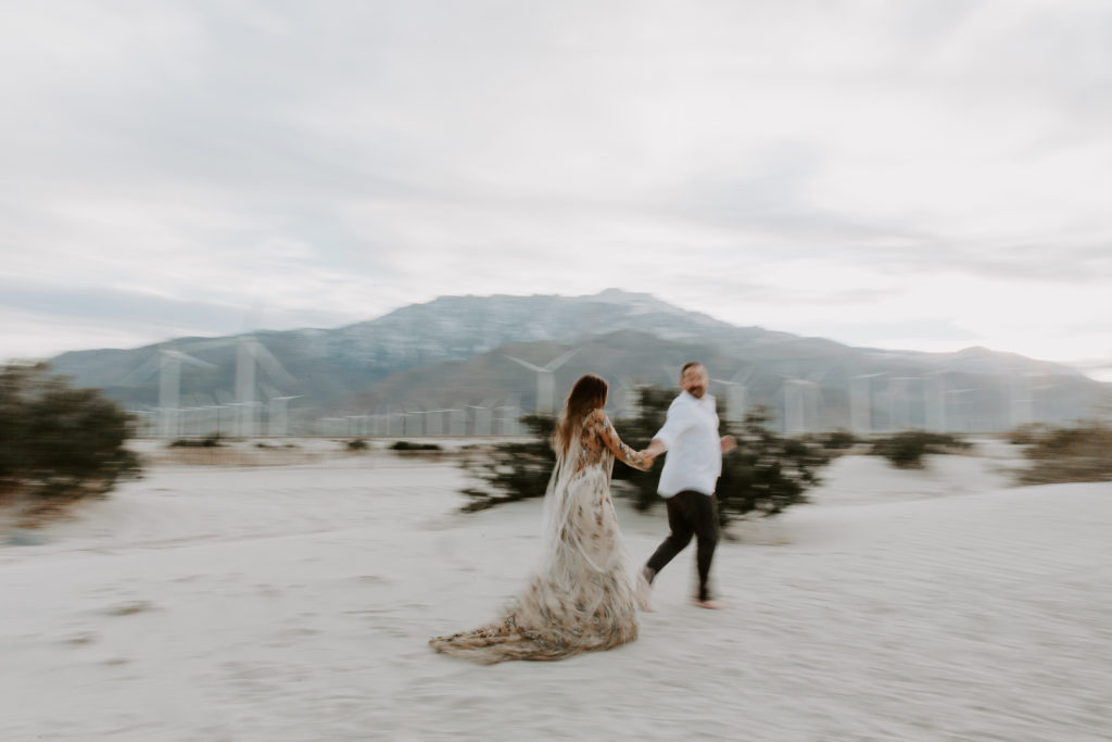 A man holding his partners hand as they run across the desert during their couple photoshoot in Palm Springs, California