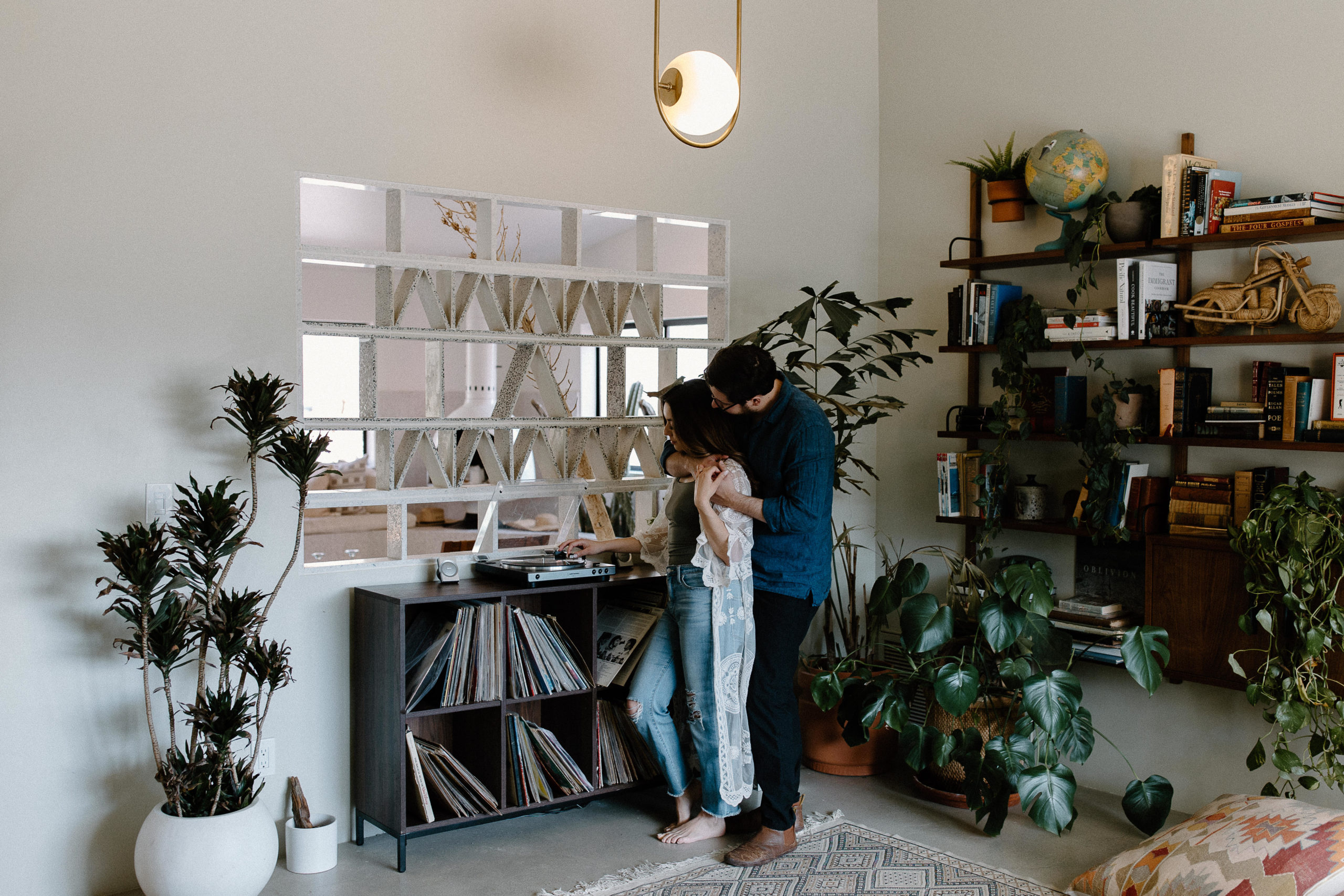 A couple standing at their record table as the man has his arms wrapped around his partner and she is placing a record during their in-home couple session in California