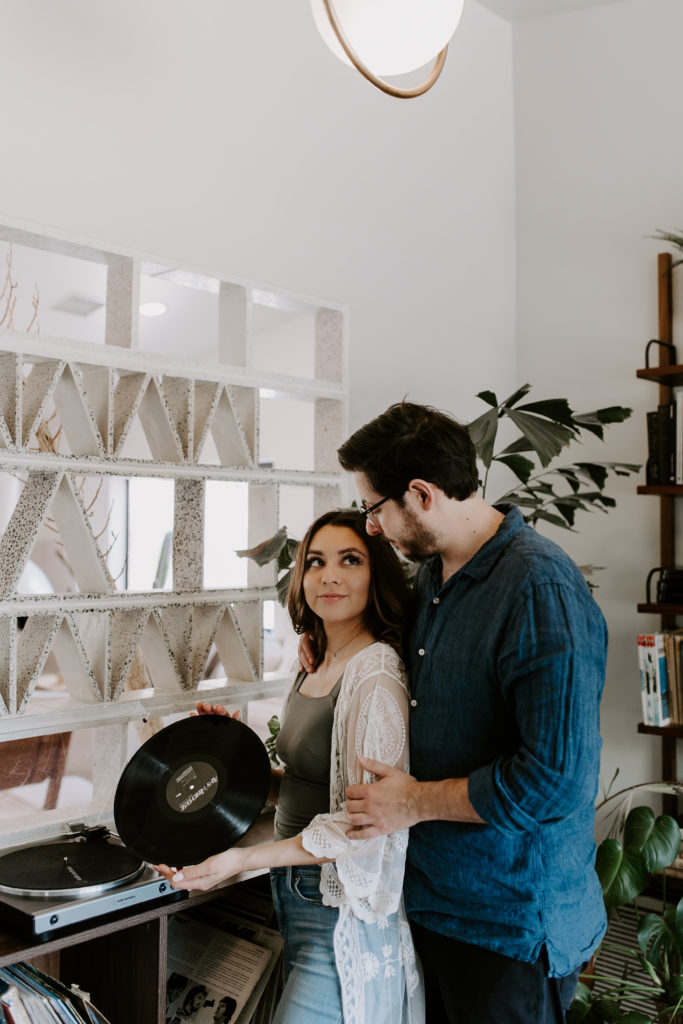 A woman looking up at her partner as she is holding a record and he is looking down at her during their in-home Palm Springs couple photoshoot