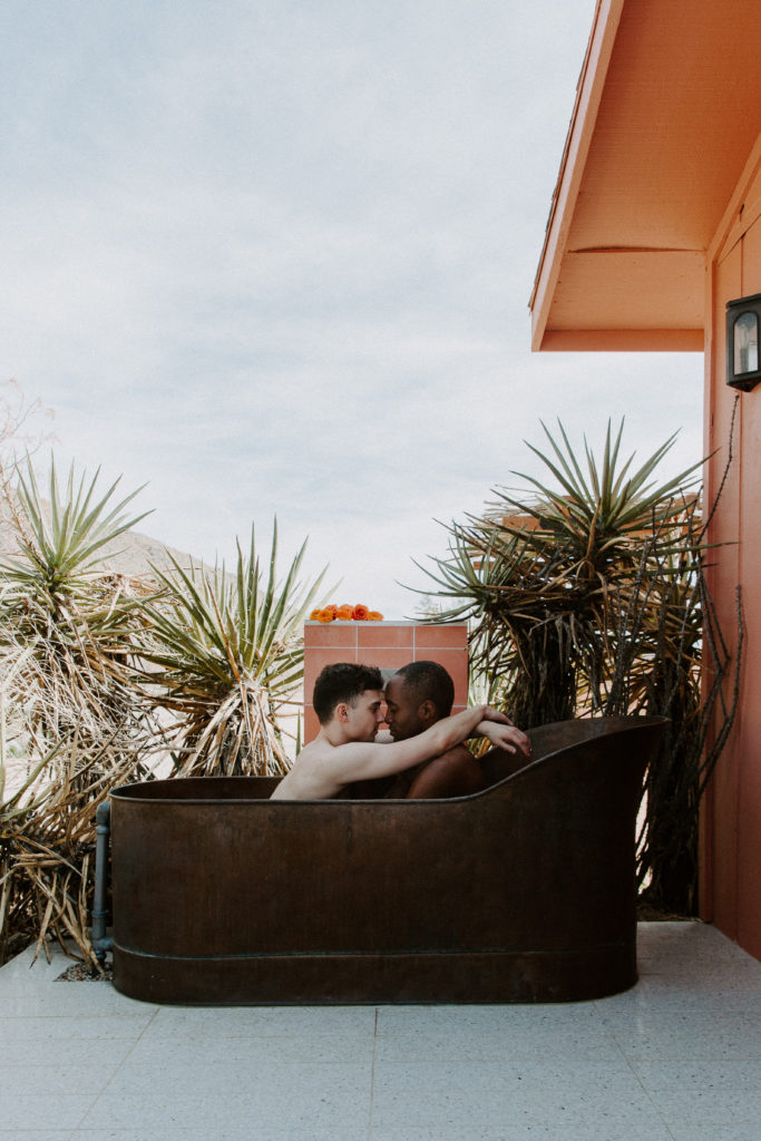 A couple sitting in an outdoor bathtub with their arms wrapped around each others shoulders during their intimate couple session in the California desert