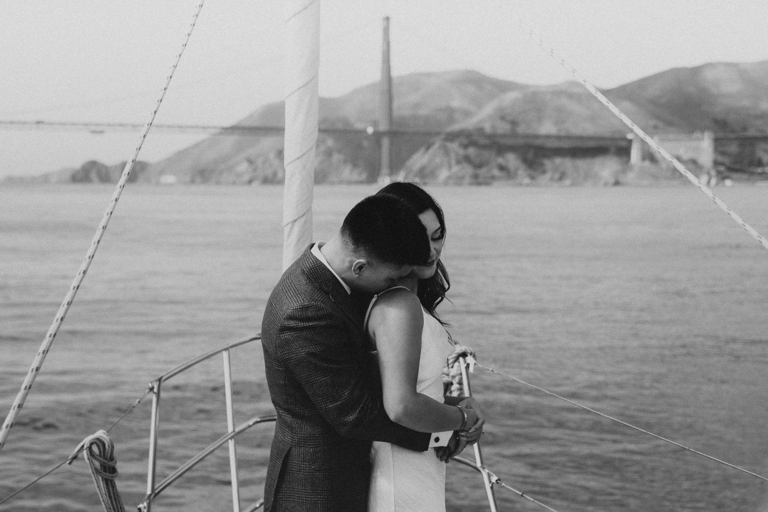 Man giving his partner a kiss on the shoulder as she holds on to his arms that are wrapped around her during their San Fransisco elopement