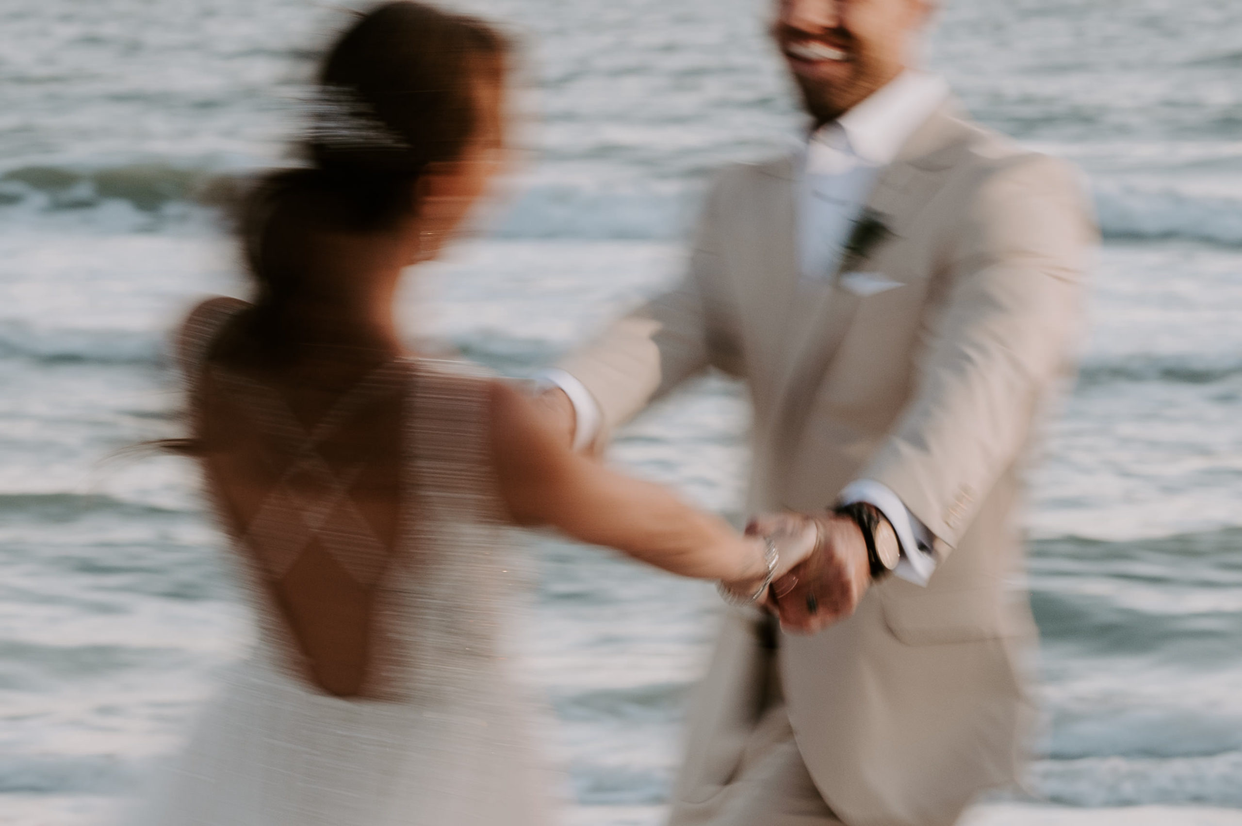 A blurry photo of a couple holding hands and swinging in circles as they are laughing on the beach at Treasure Island