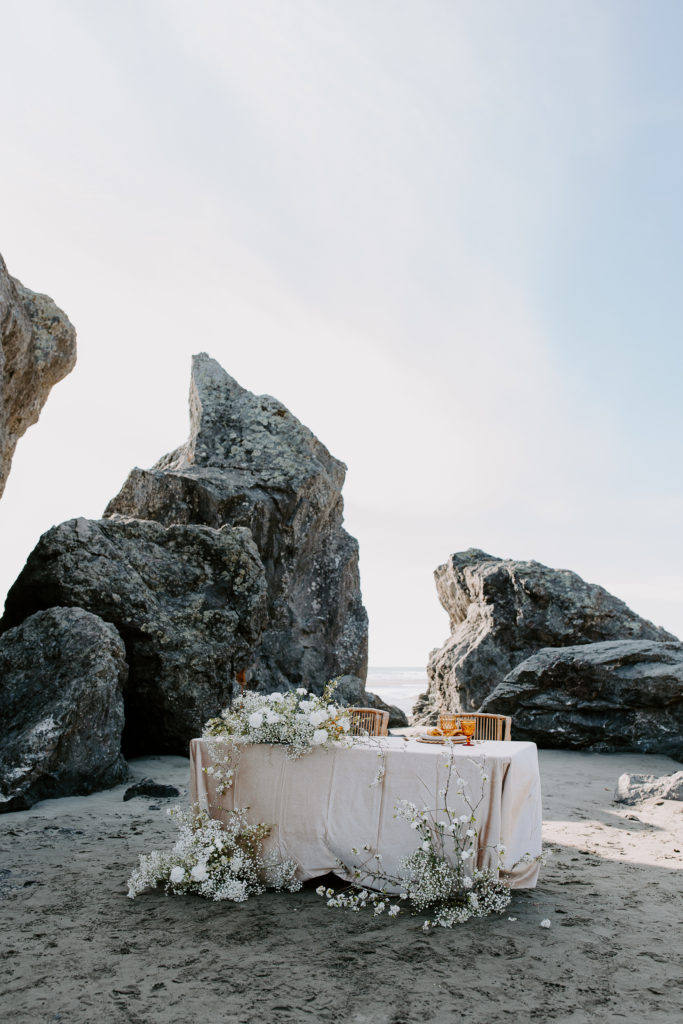 A wedding table with pink tablecloth, orange glasses and babys breath for a beach wedding in Northern California