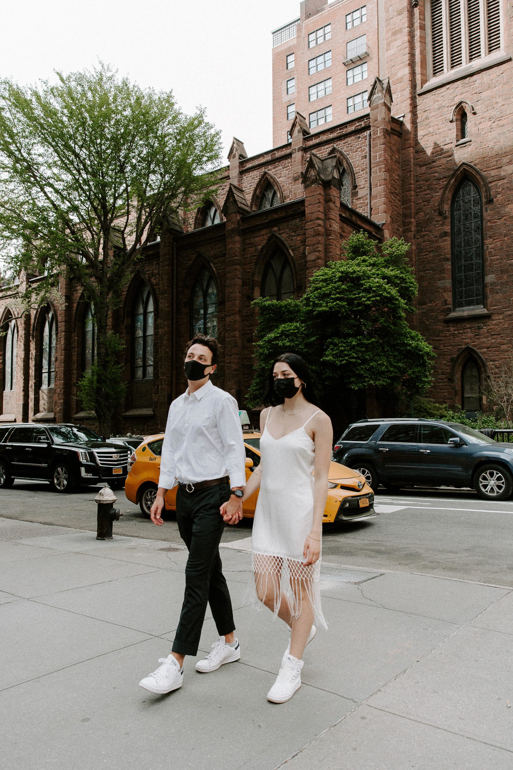 A couple in wedding attire holding hands and wearing face-masks during their COVID urban elopement