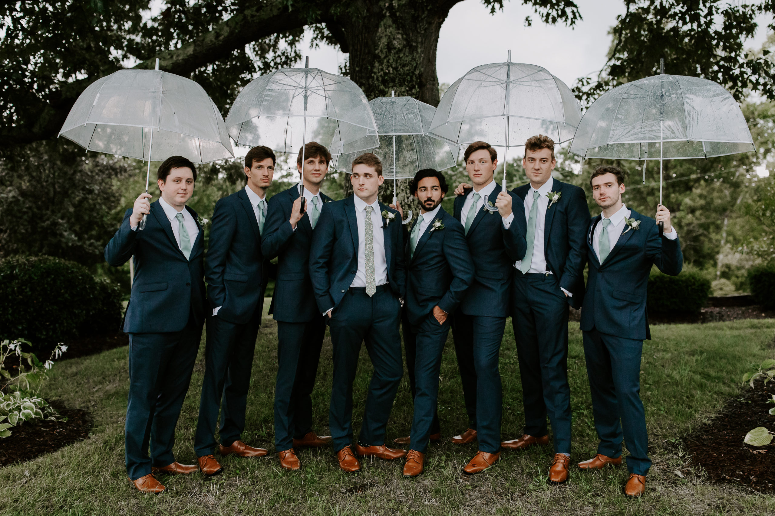Groom and his groomsmen all in blue suits holding umbrellas and looking of fin to the distance during a rainy wedding in Tennessee