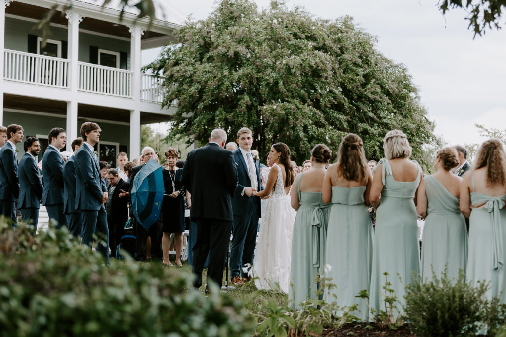 A bride, groom and their wedding party all standing up under a large tree during the outdoor wedding ceremony in Nashville