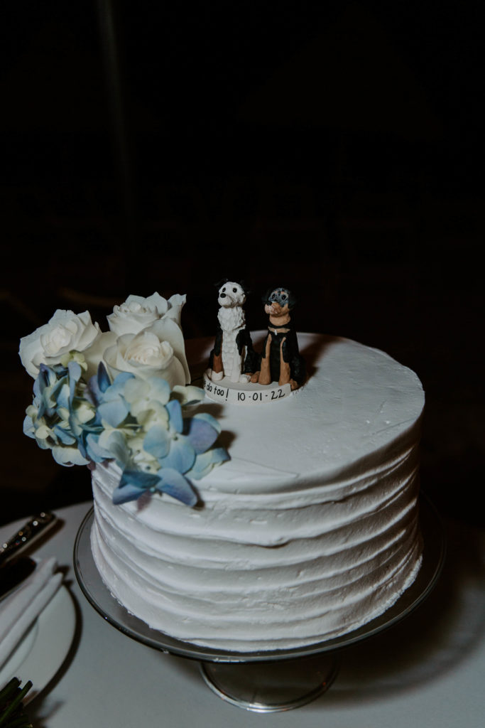 Simple white wedding cake with blue flowers and a dog cake topper