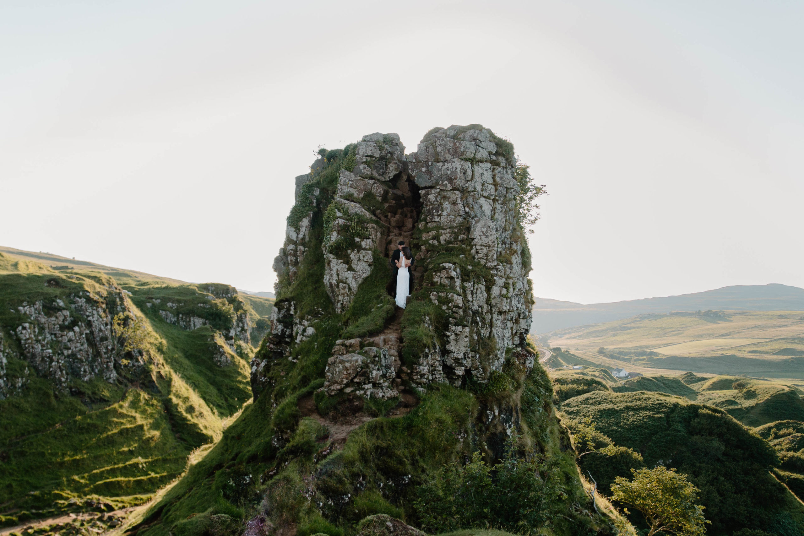 A couple standing as they embrace each other in a large rock cliffside cut out and the sun is setting behind them during their Scotland adventure elopement in the Isle of Skye