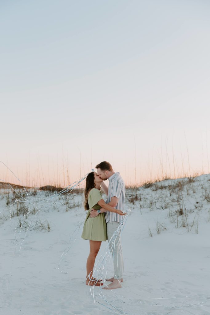 A newly engaged couple sharing a kiss and popping streamers as they celebrate their engagement during their beach photo shoot in Destin Florida