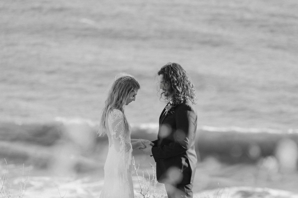 A couple standing on the edge of a set of cliffs overlooking the ocean saying their vows during their Malibu elopement