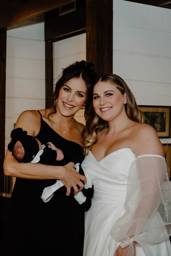 A bride standing with her sister who is also her maid of honor who is holding her three week old daughter during a Florida winter wedding in the panhandle