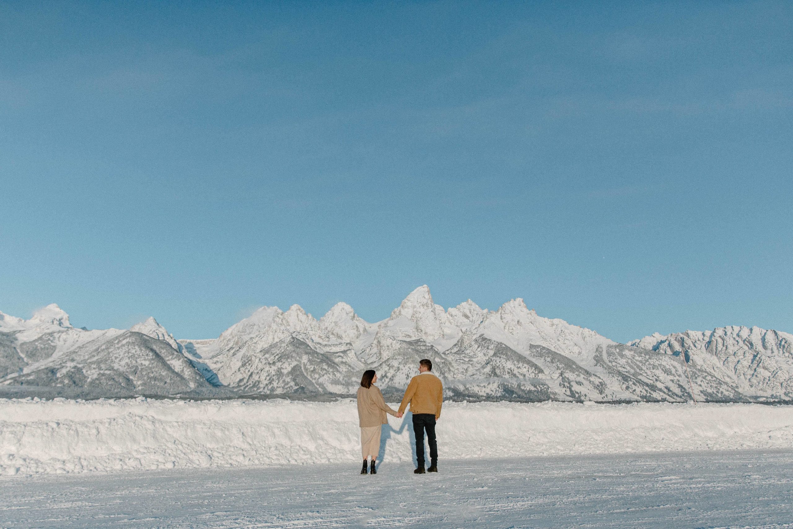 A couple holding hands and facing the mountains as the sun rises during their couple photo shoot in Grand Teton National Park
