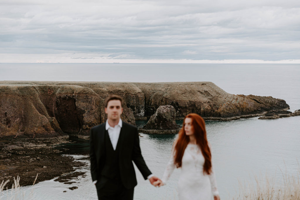 A couple standing holding hands while in their wedding attire on a gloomy day in Scotland during their all day adventure elopement in Stonehaven