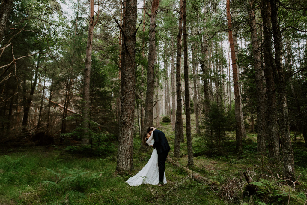 A man dipping and kissing his partner in a wooded forest in Inverness during their adventure Scotland elopement