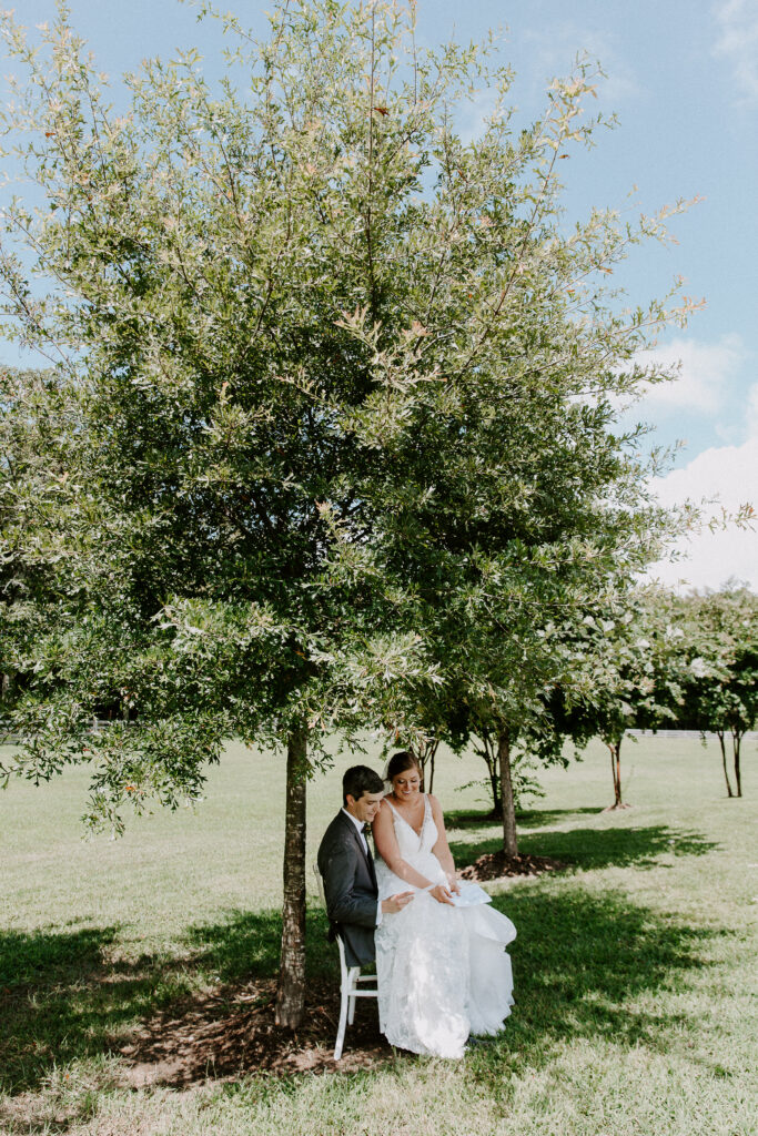A woman sitting on her partner's lap in their wedding attire as they are sitting under a tree reading private letters they wrote to each other on their wedding day during their fall Tennessee wedding in Chattanooga at Howe farms