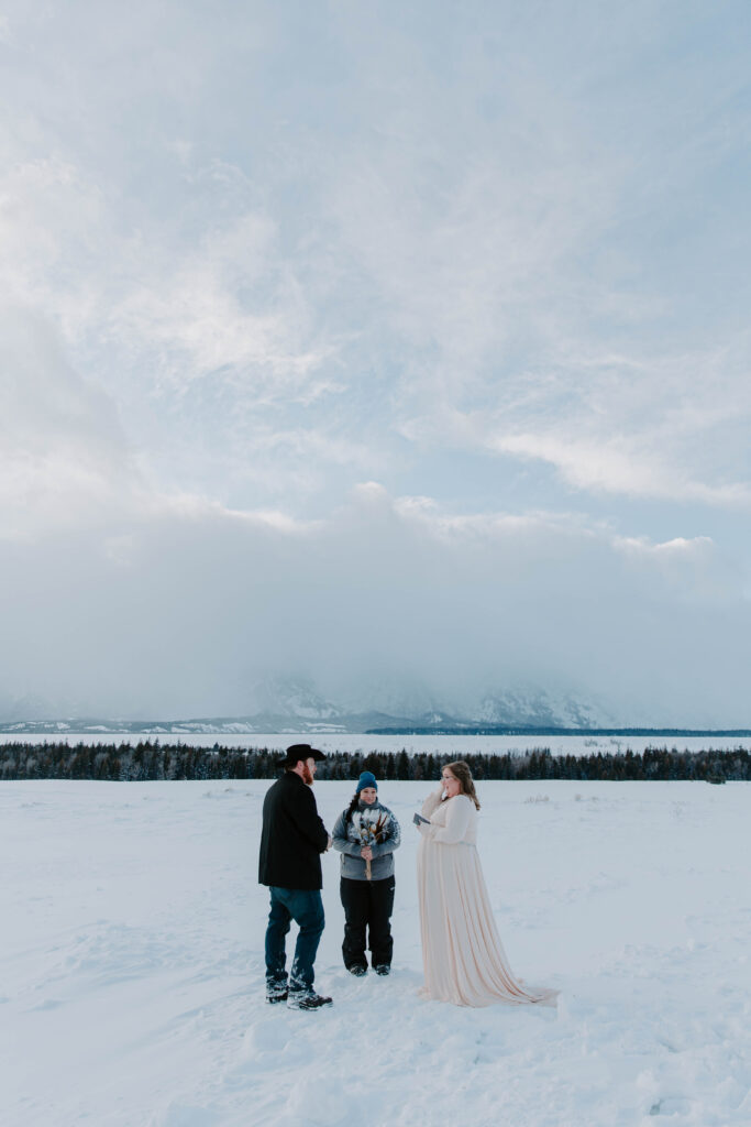 A couple standing close together sharing their battles with one another with grand Teton national Park in the background during their winter Wyoming wedding
