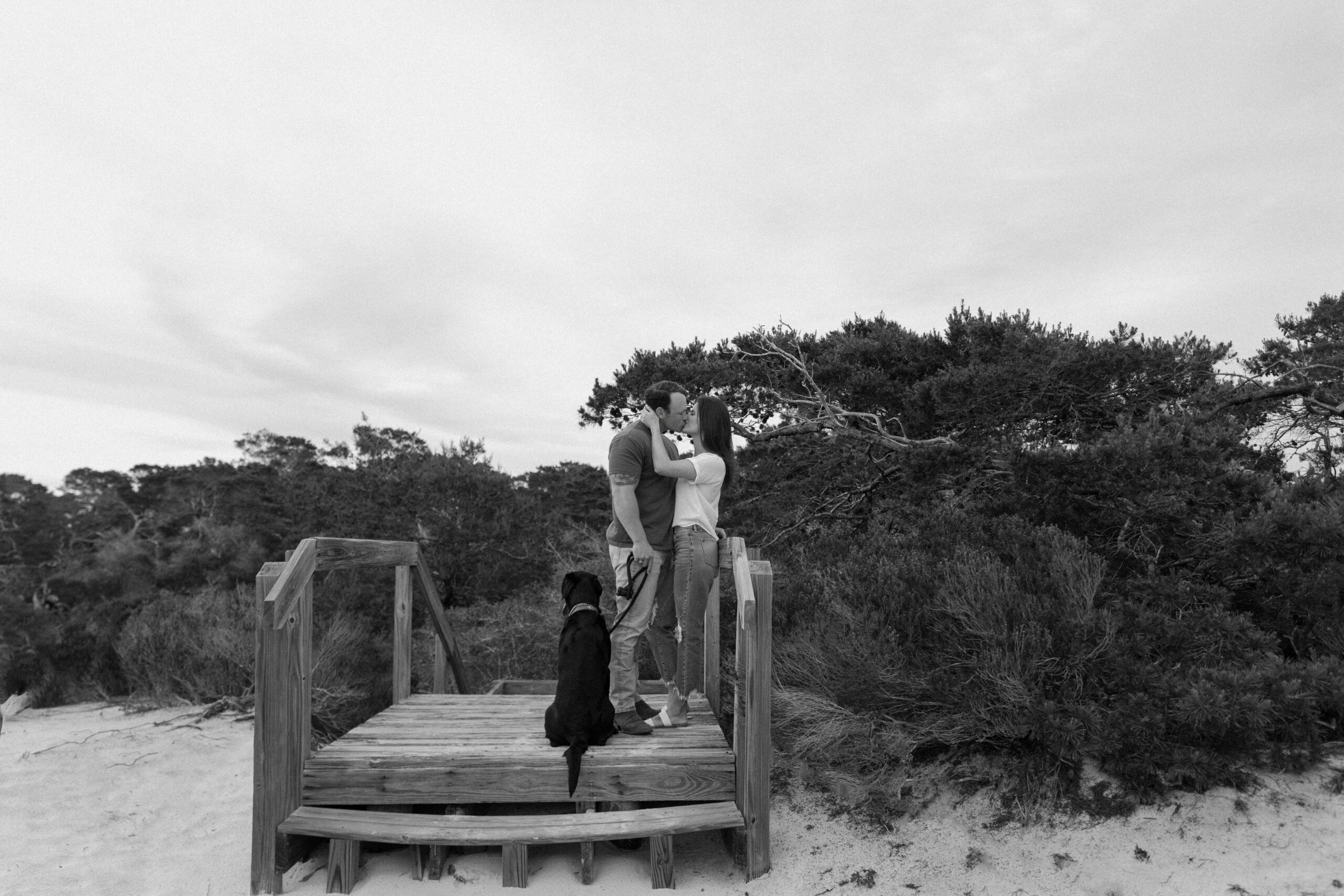 A couple embracing on a bridge as their dog sits next to them and looks off into the distance during their Henderson Beach State Park couple photos in Destin