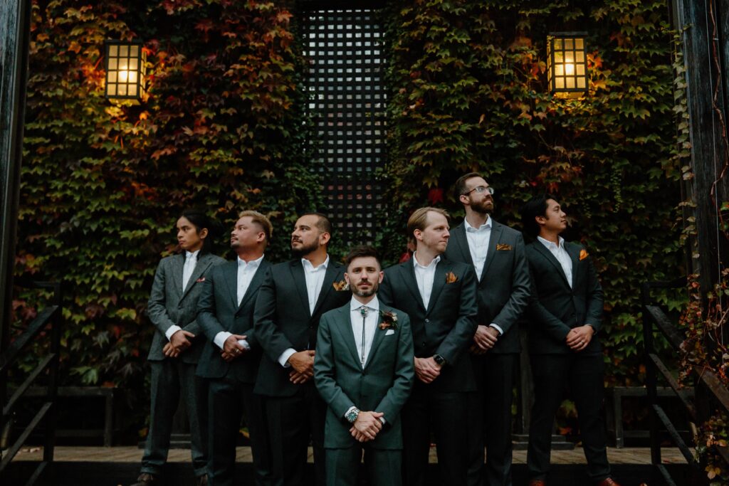 A groom and his groomsmen standing on steps with the groom in the middle and the other men surrounding him looking in different directions during his Queens, New York wedding