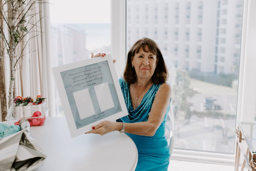 Mother of the groom holding up a picture frame that she will eventually be able to put wedding photos in during her sons Florida Panhandle wedding