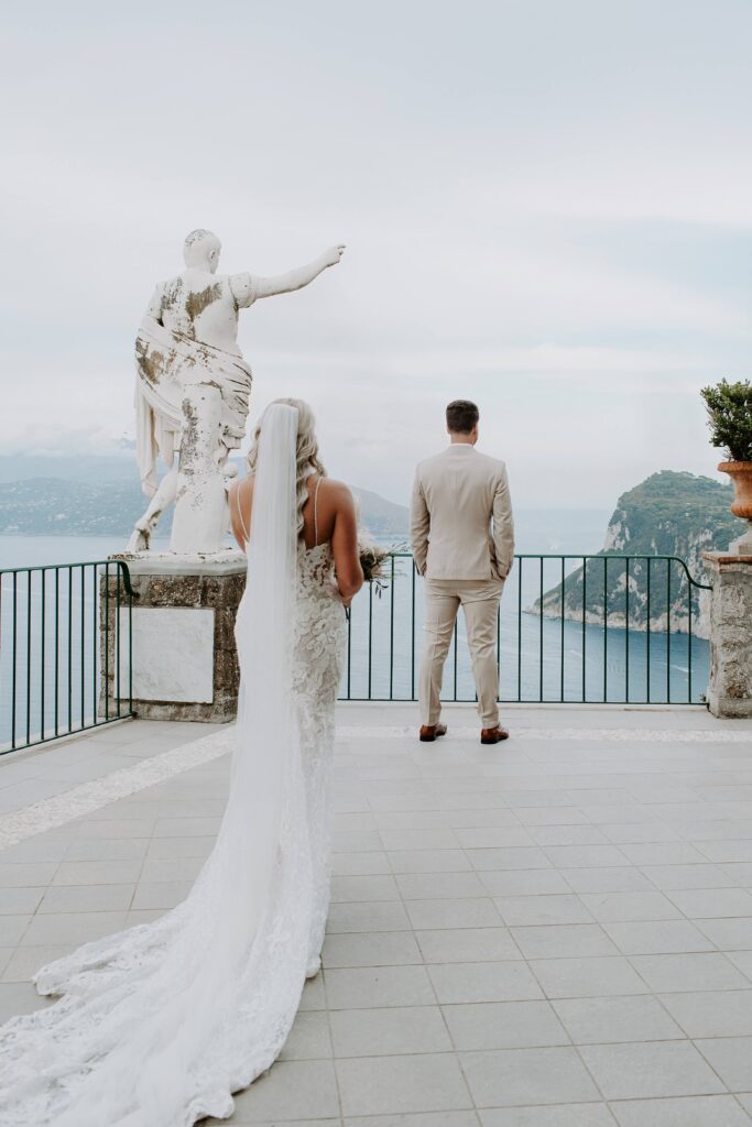 A woman walking up being her partner as they get ready for their first look on a terrance overlooking the sea in Capri during their Amalfi Coast wedding