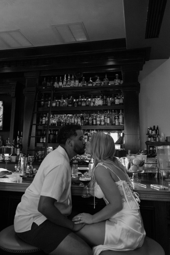 A couple sharing a kiss as they sit at a bar with espresso martinis during their 30-A engagement session in Rosemary Beach