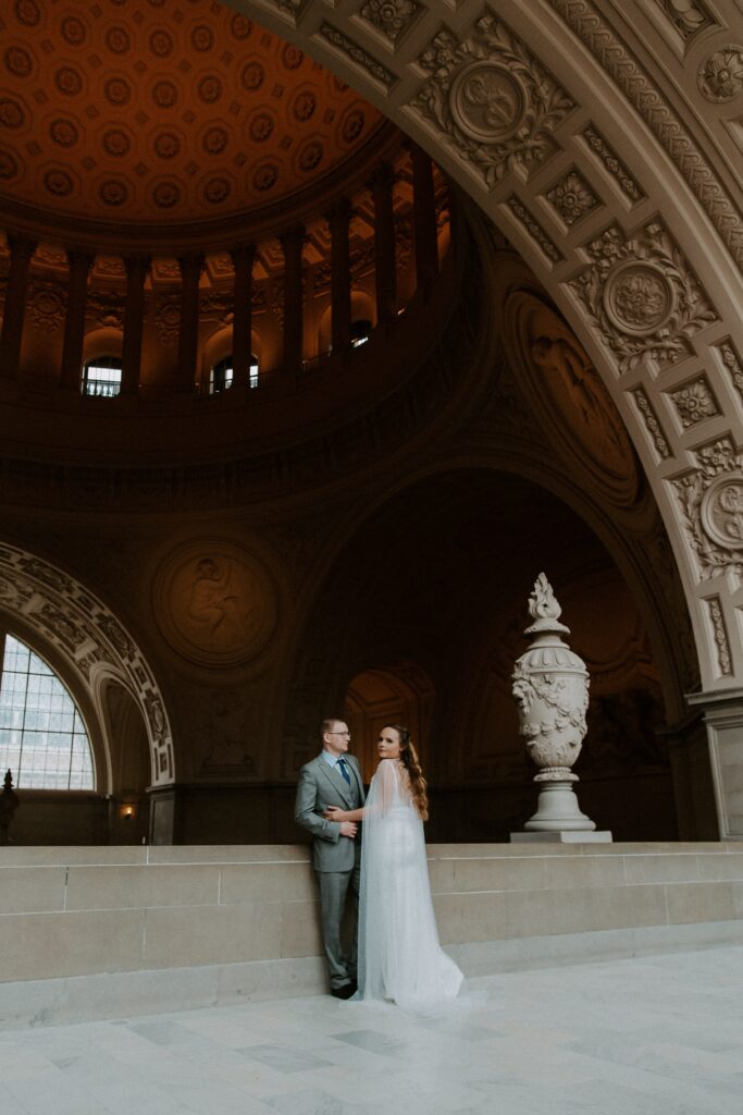 A couple in wedding attire leaning up against the railing in City Hall after saying their vows to one another during there all day California elopement in San Francisco