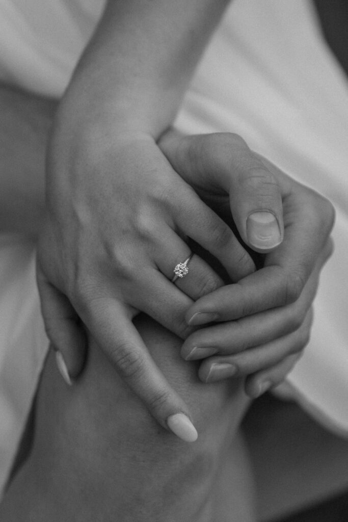 A woman resting her hand on her knee with her partners hand resting on her thigh with her new engagement ring on her finger during their middle Tennessee engagement photos in Nashville