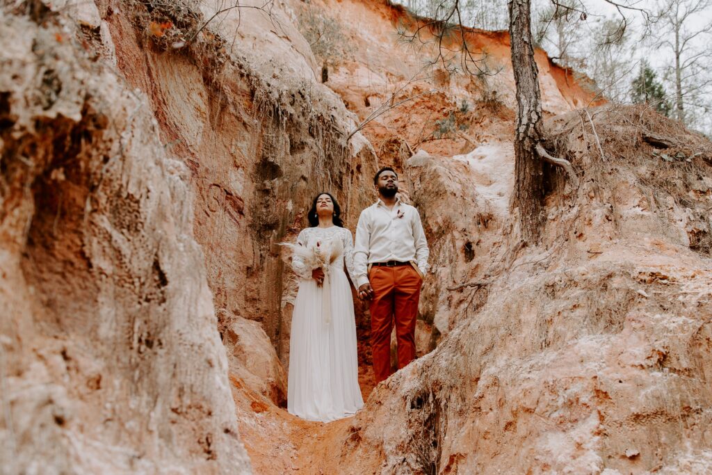 A newly wed couple holding hands and looking up at the sky with their eyes closed as they stand in Providence Canyon during their Georgia elopement