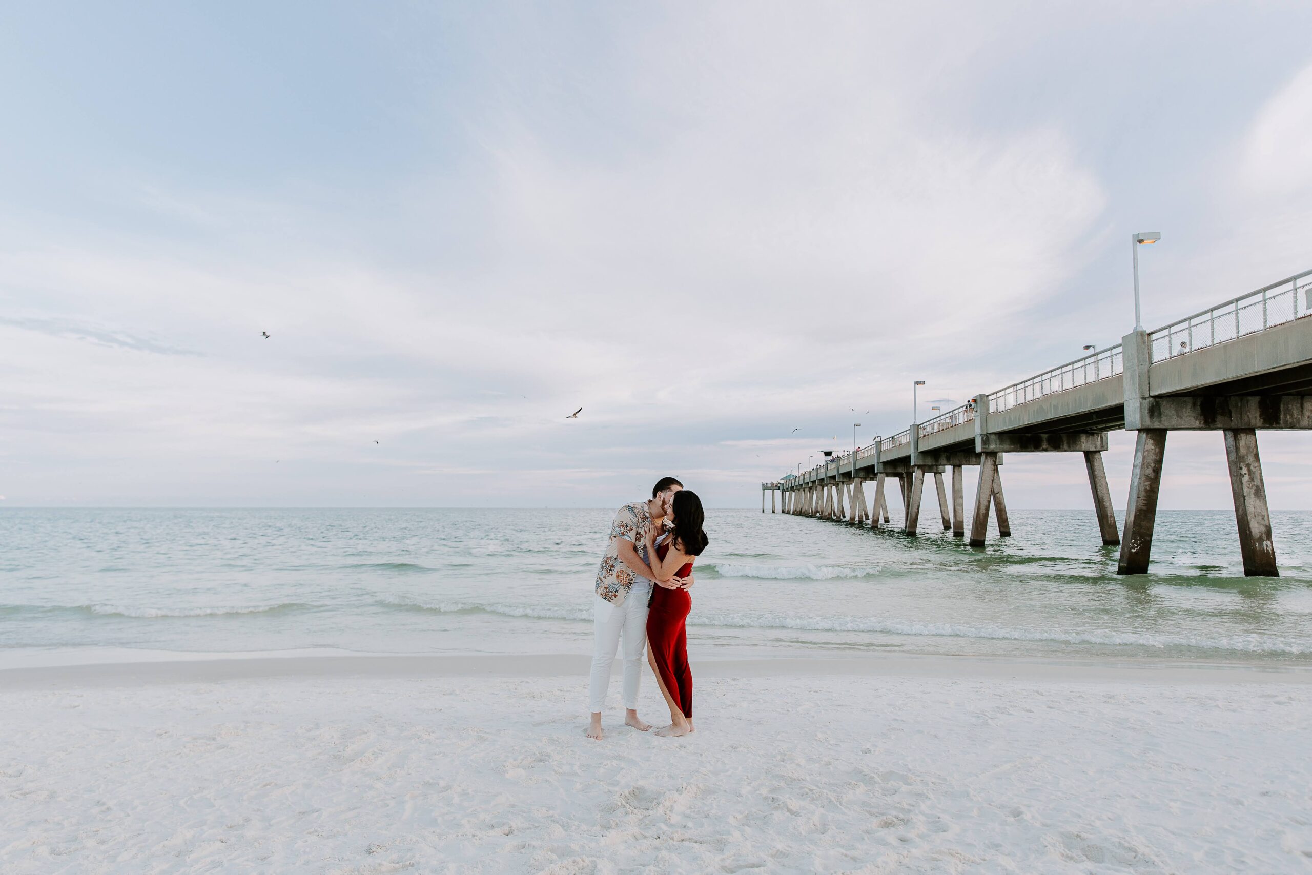 A woman embracing with her partner as the sun sets and the birds fly overhead during their beach engagement photos in Destin