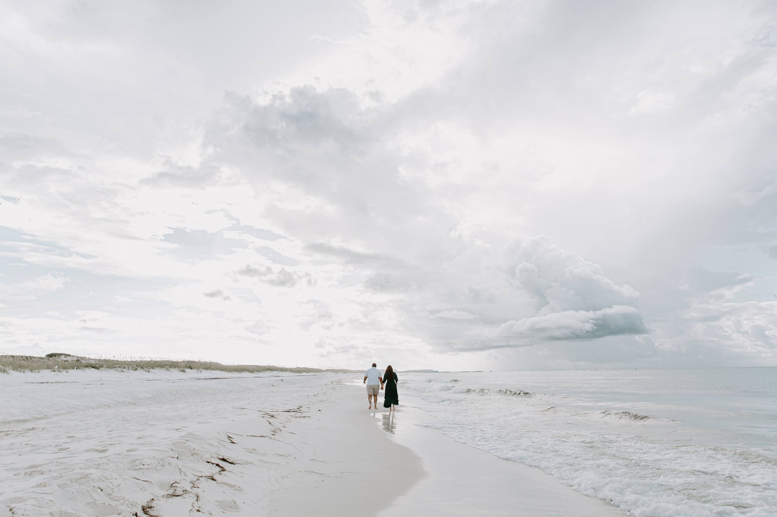A couple holding hands and running down the beach as a storm starts to brew over the ocean during their sunrise couple photos in Desitn