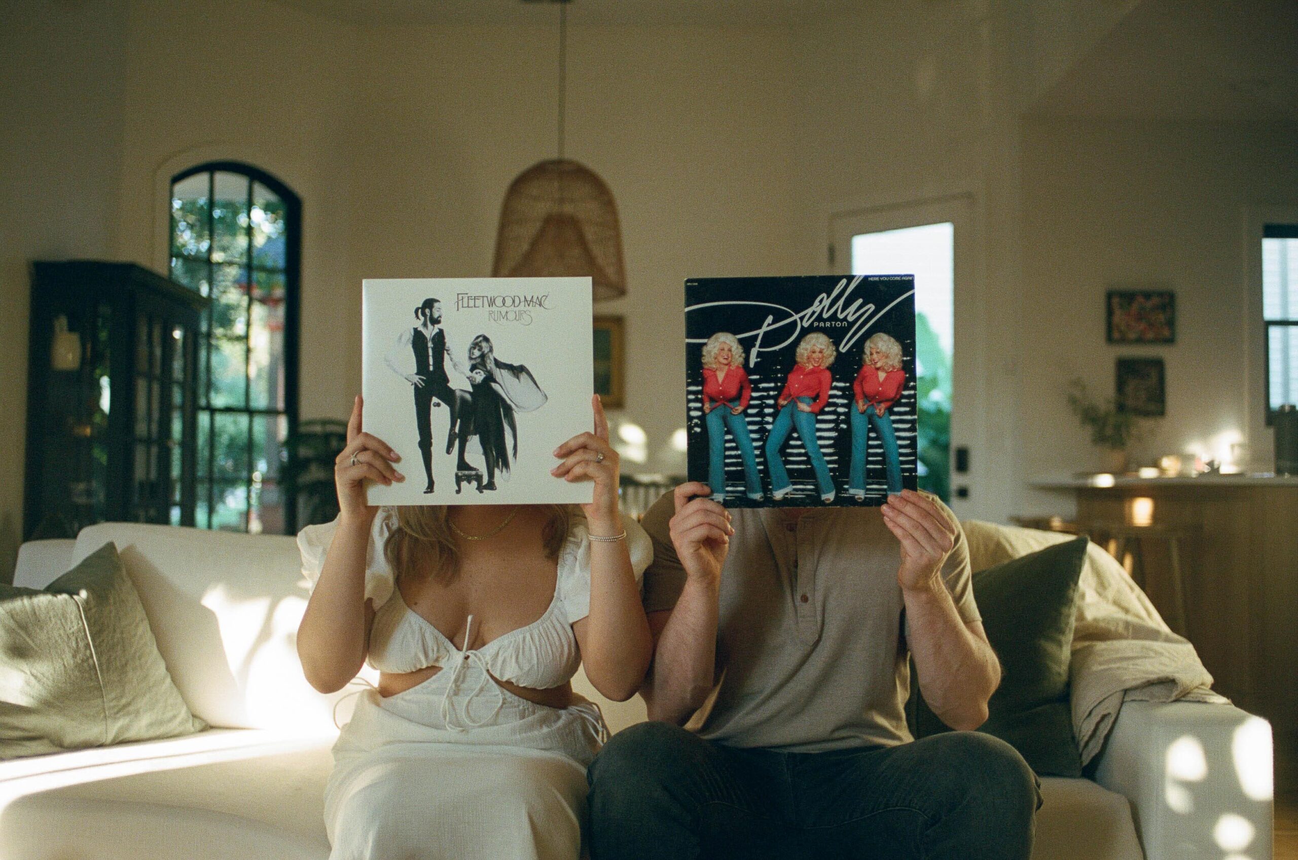 A man and a woman holding their favorite records in front of their faces as they sit by side on their couch during their Tennessee engagement photos