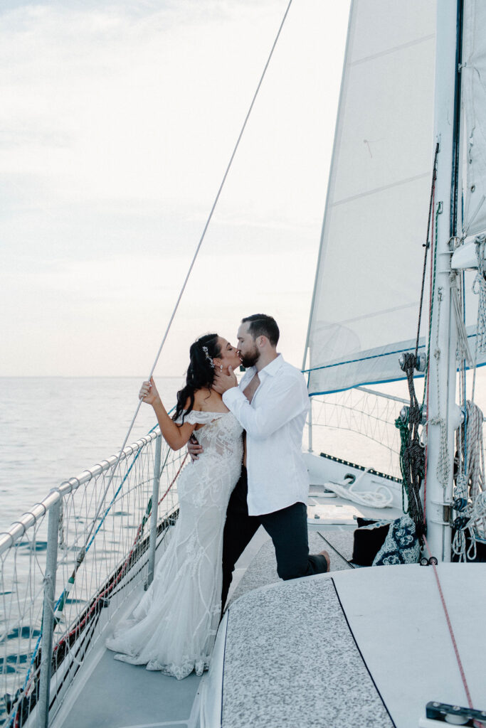 A couple standing at the front of a sailboat as the woman holds on to the side and the man brings her in for a kiss during their sailboat elopement in Key West