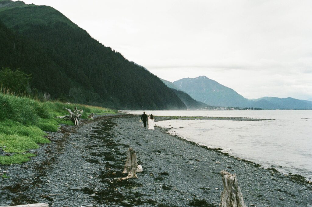 a couple holding hands and walking along a black beach in seward alaska during their all adventure elopement