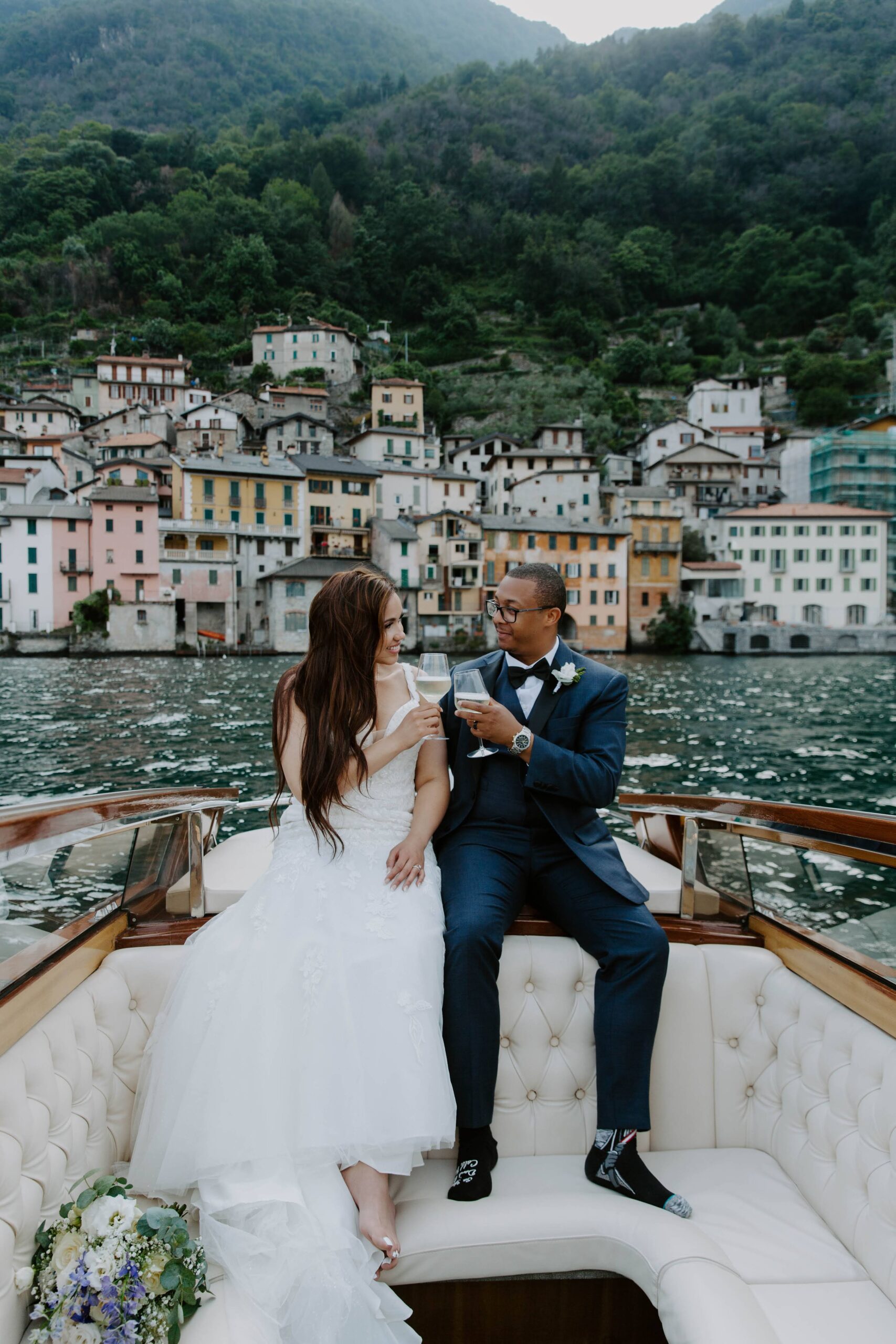 A newly wed couple sitting on the back of a boat on Lake Como as they toasts to their italy wedding