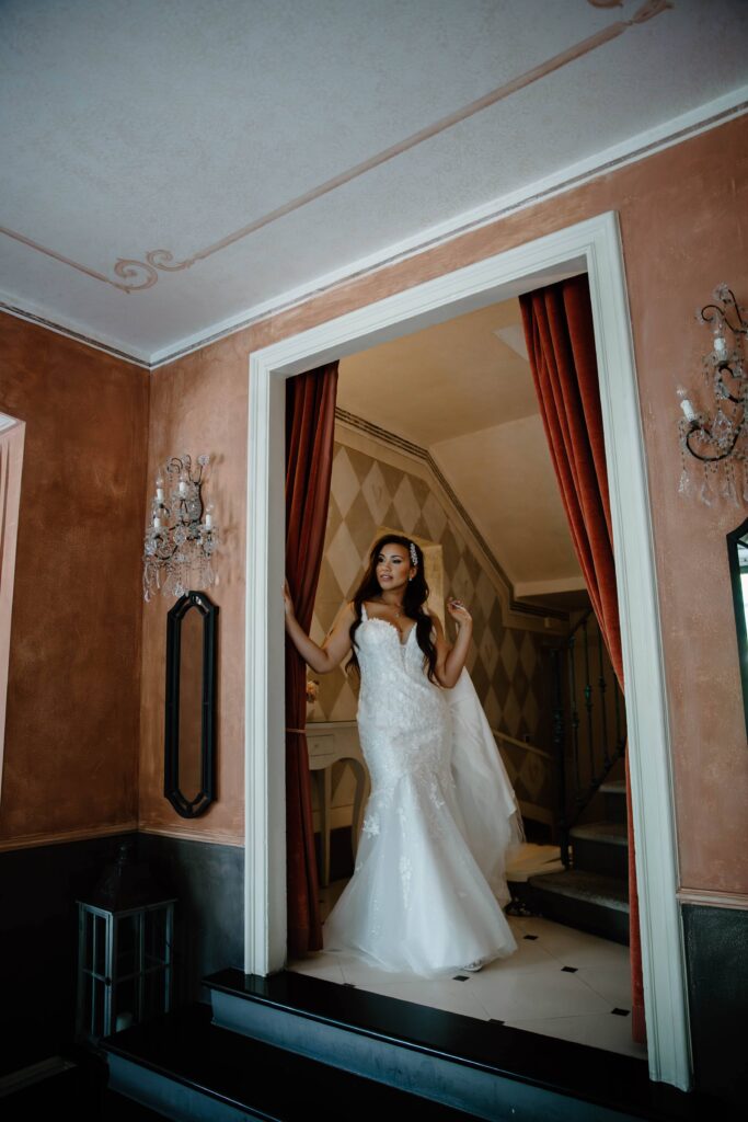 A woman standing in a doorway holding her wedding dress as she looks out over lake como during her italy wedding