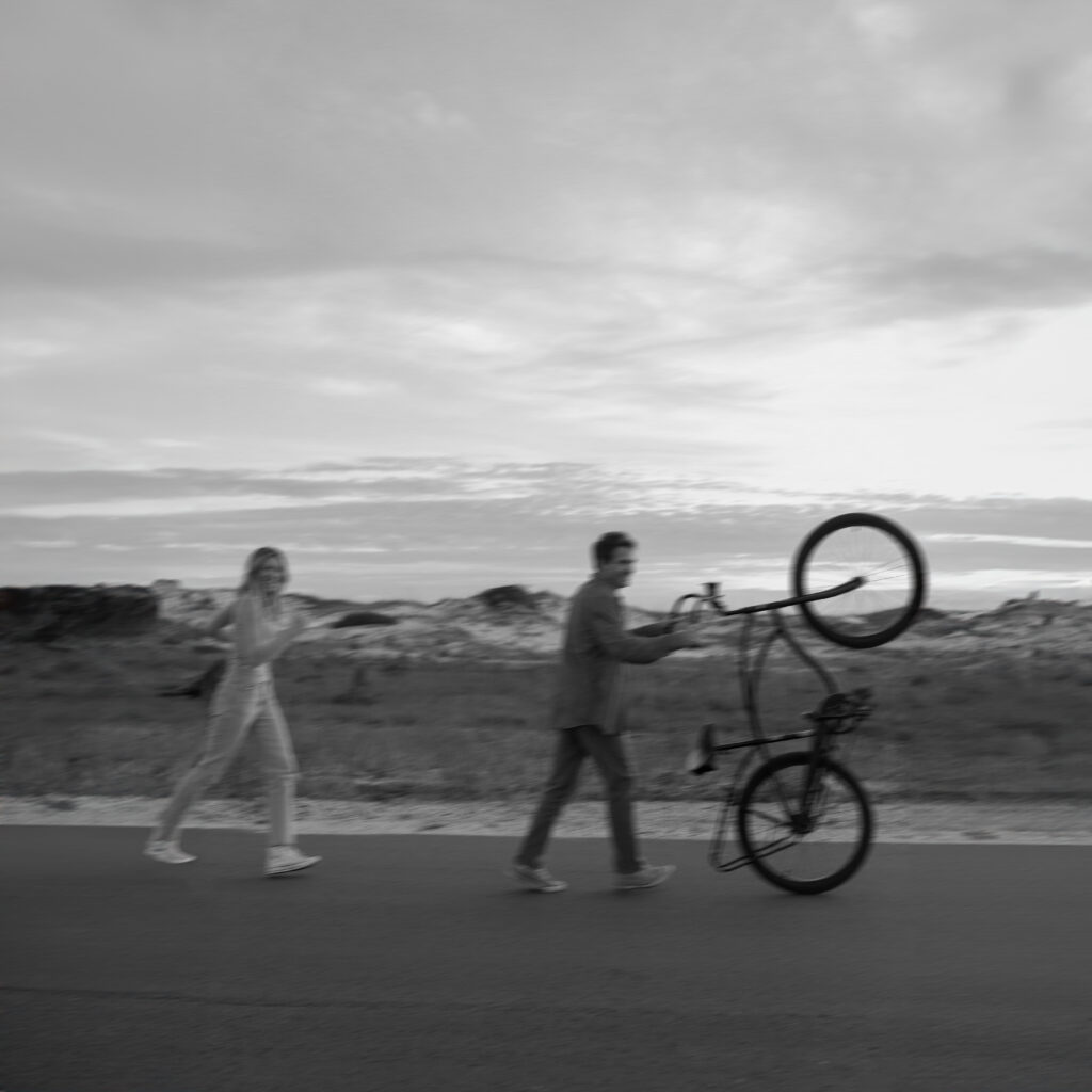 A man running while holding up a bike as his partner runs behind him during their beach engagement photos in Florida