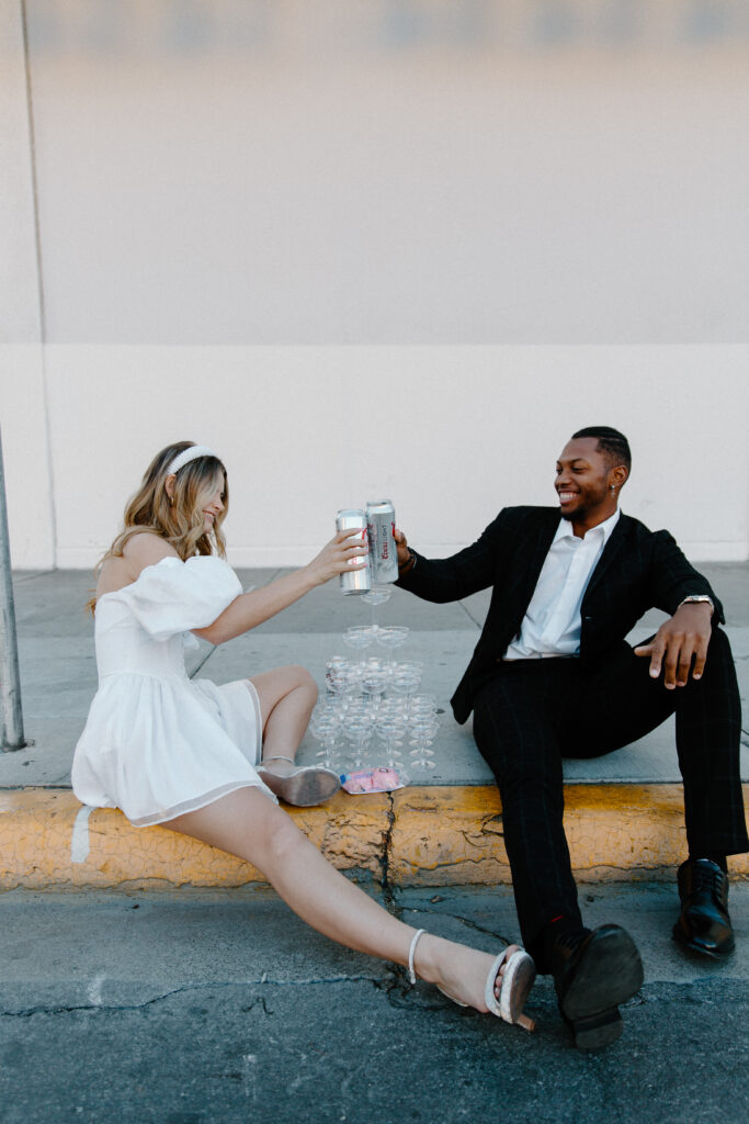 A couple in wedding attire with a champagne tower in between them and toasting their beer cans during their Las Vegas wedding