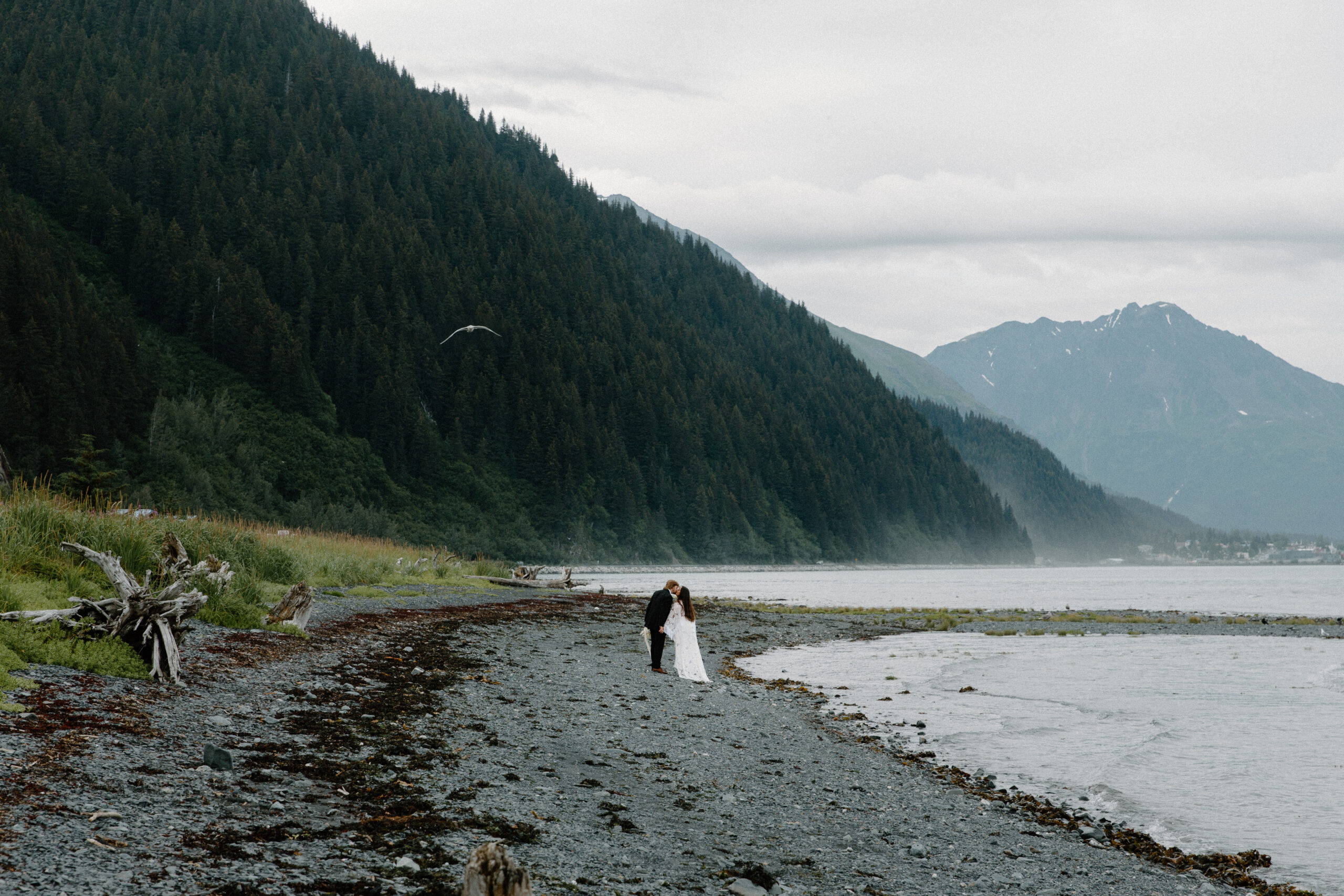 A couple sharing a kiss with the Alaskan mountains, rising in the background during their summer elopement in Seward