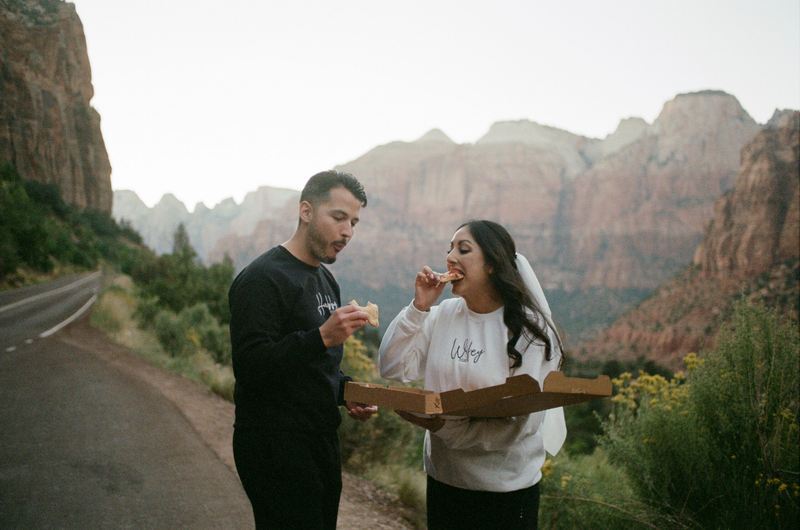 A woman taking a big bite of pizza as her partner is chewing during their adventure elopement in zion national park