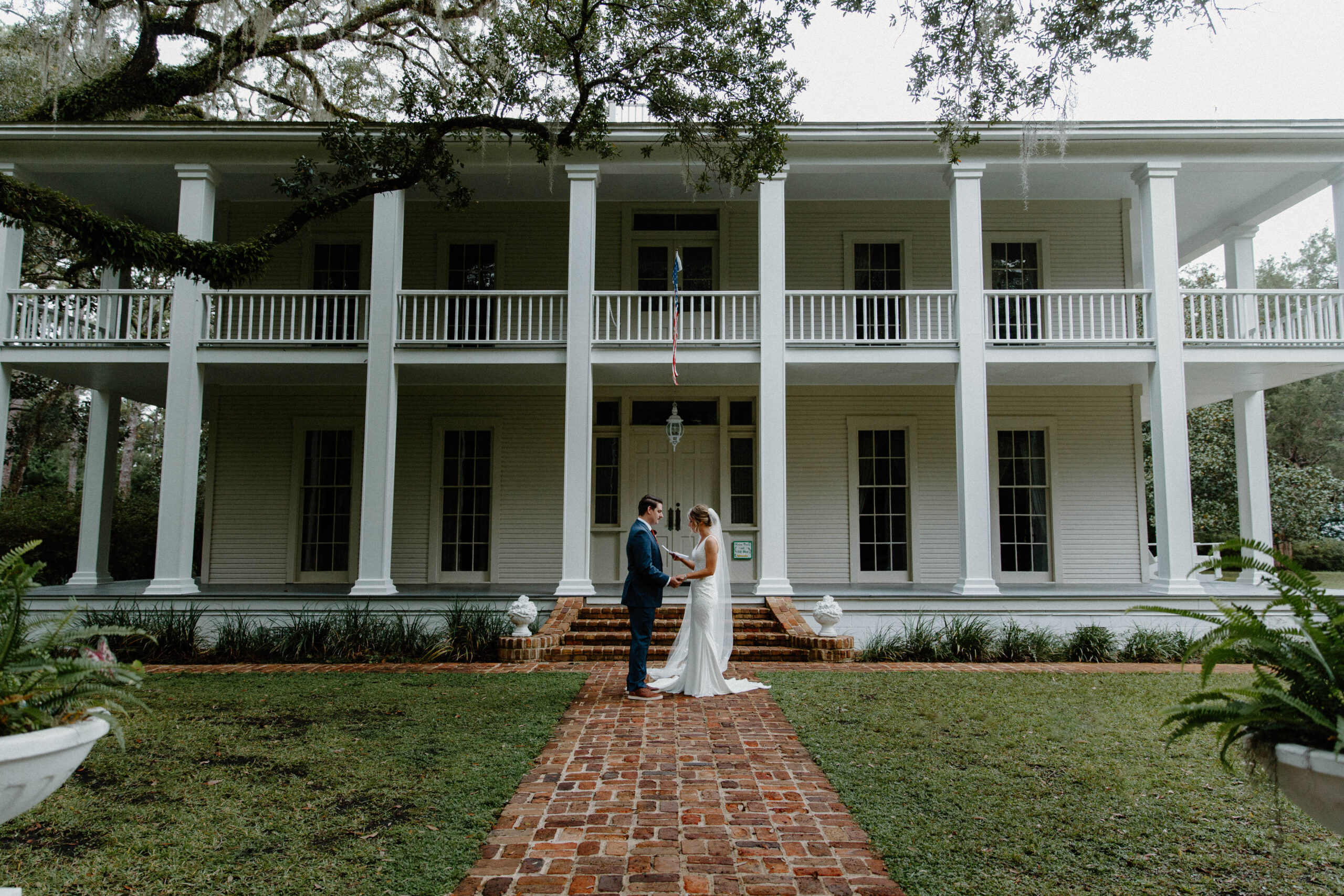 A couple reading private vows to each other in front of a large white house at eden gardens state park