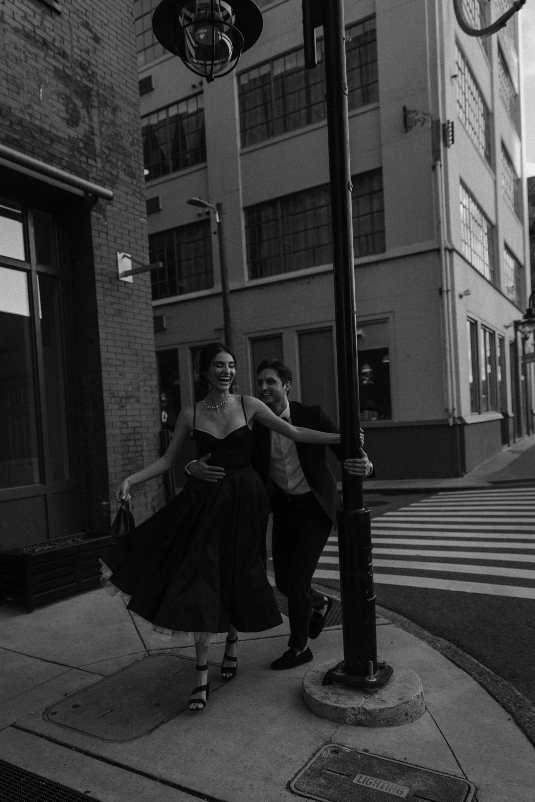 A woman holding onto a light post running in circles around it as your partner tries to catch her during their old city engagement photos in Knoxville Tennessee