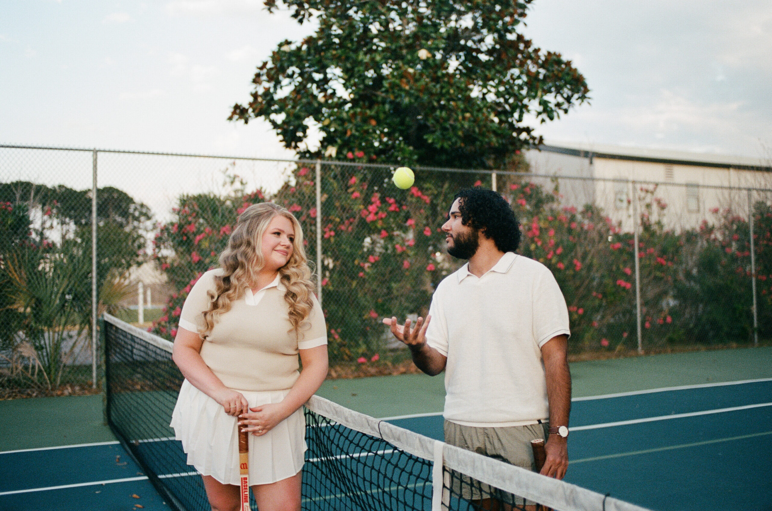 A man tossing up a tennis ball as he looks at his partner and she looks at him during their Florida couple photoshoot