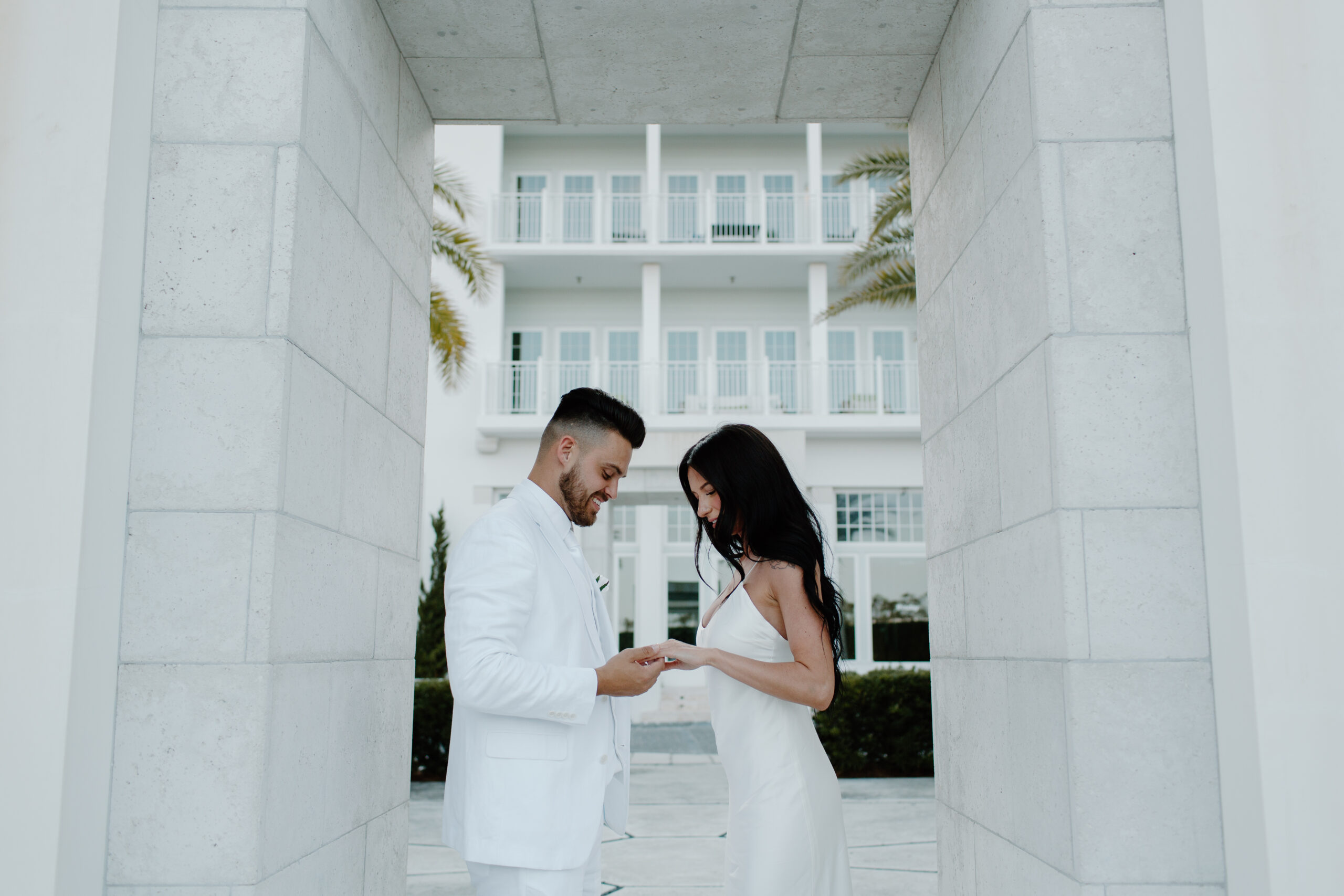 A man holding his partner's hand as they both looked down at the ring, he just placed on it during a Florida proposal on 30 A