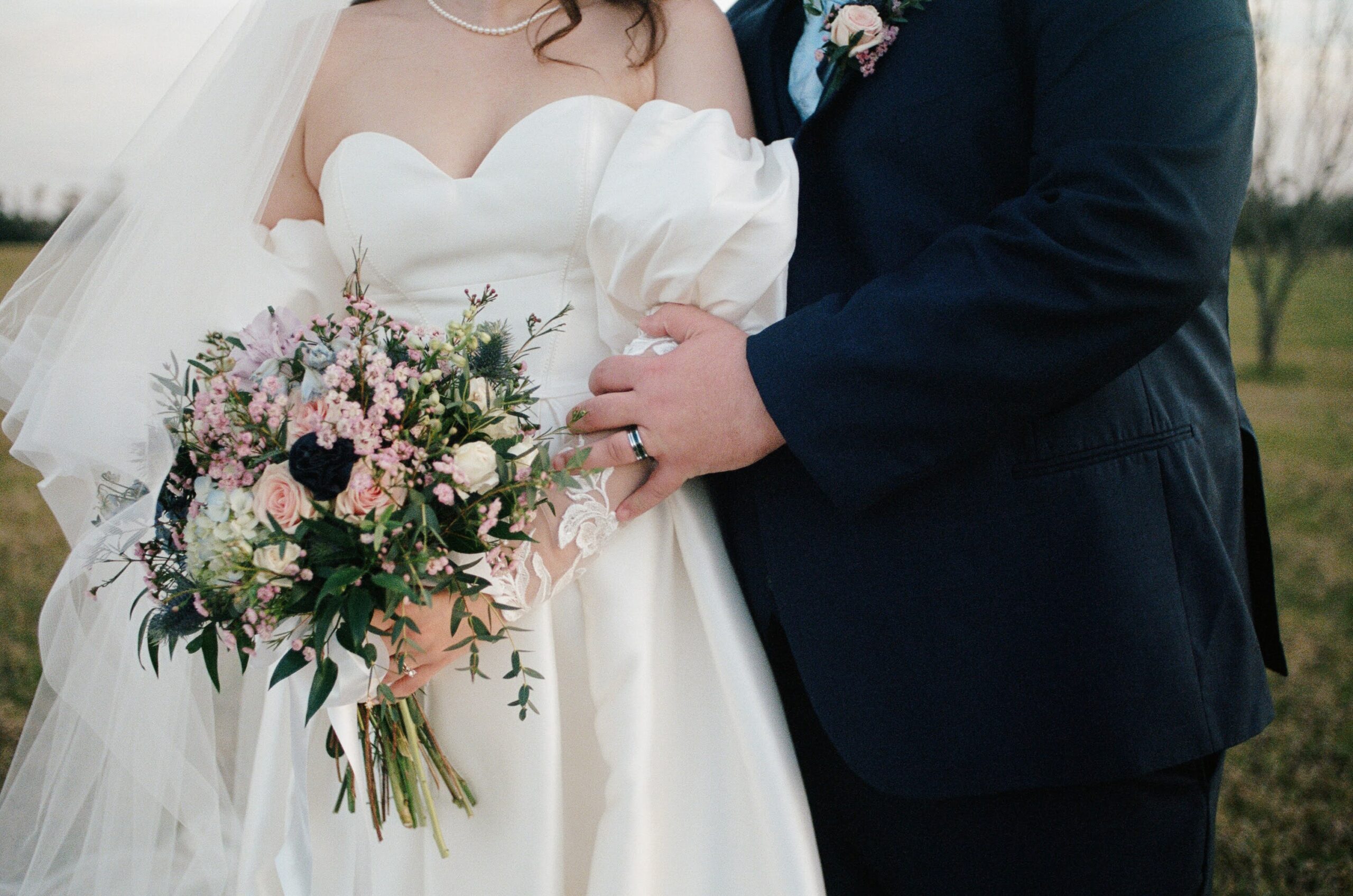 A woman in a wedding dress holding a colorful bouquet as her husband rests his hand on her arm during their spring wedding in Florida