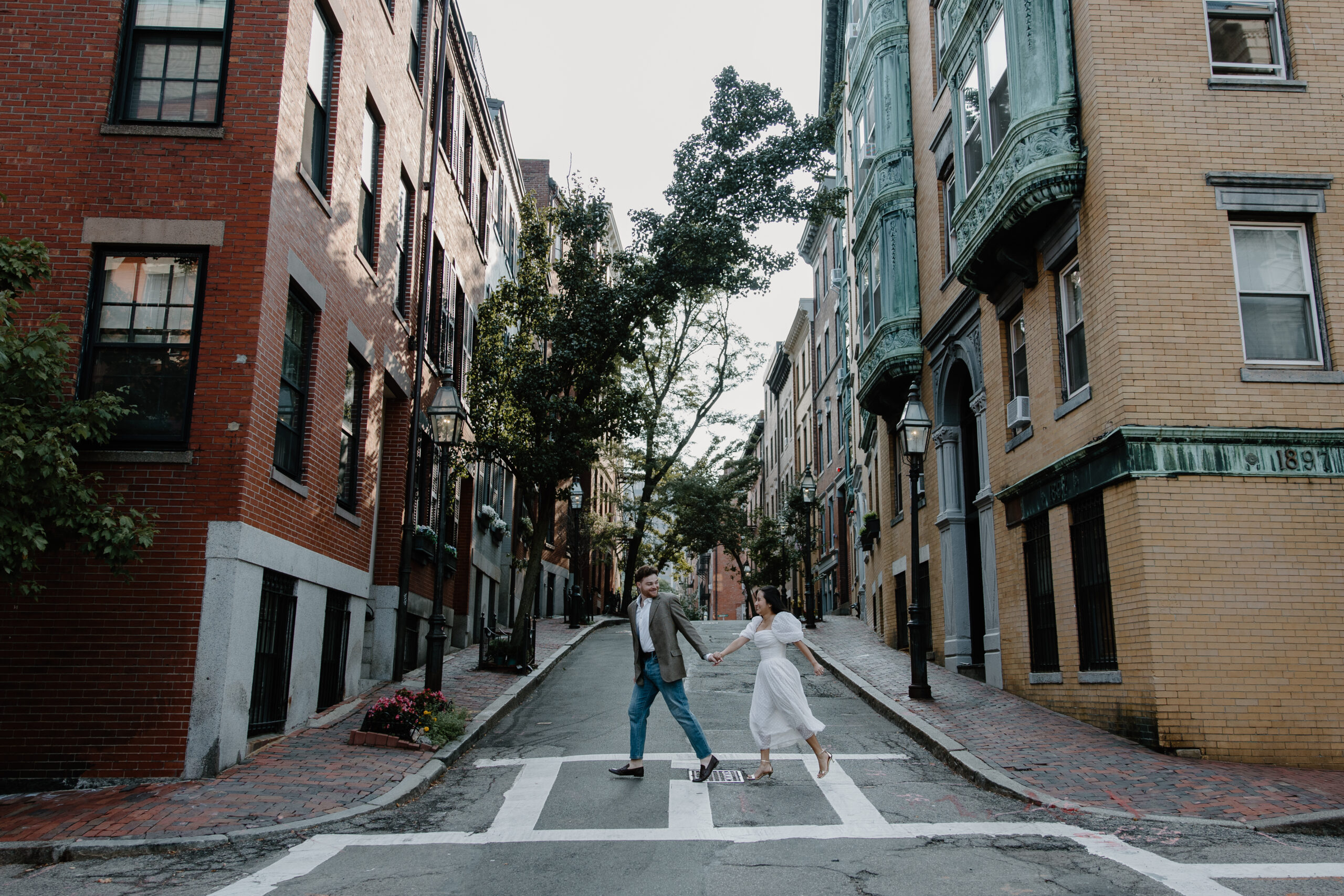 A man leading his partner across a crosswalk running during their couple photos in Beacon Hill