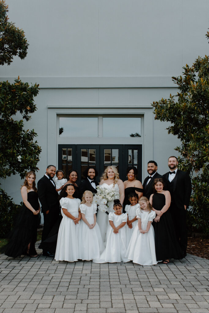 A wedding party all standing together the bridesmaids in black dresses and the groomsmen in black suits during a rainy Florida wedding