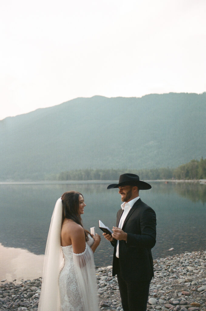A couple saying vows to each other at the waters edge in Glacier National Park during their sunrise Montana elopement