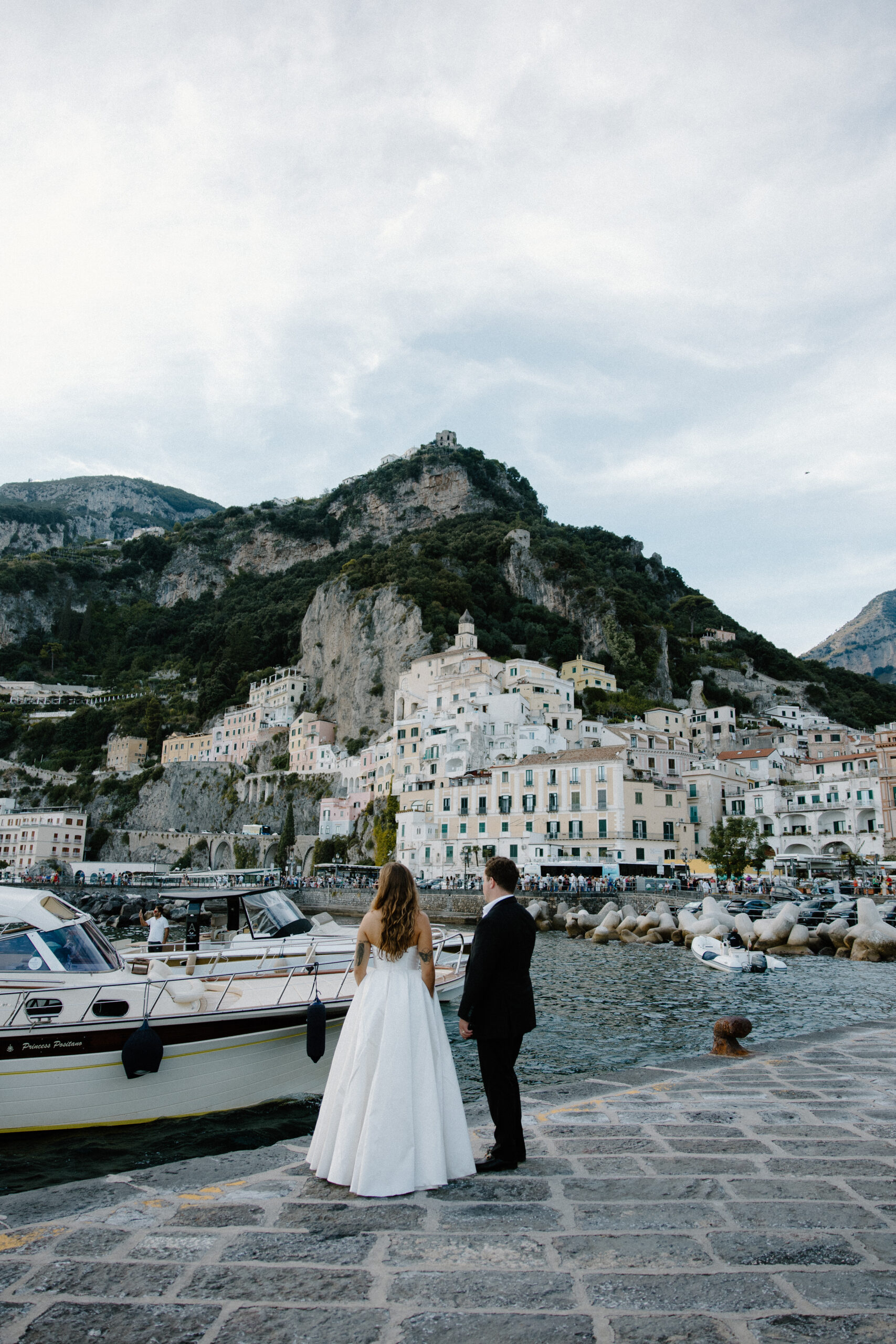 A couple standing on a stone dock as they wait for their boat at the edge of Amalfi during their Italy elopement in the fall