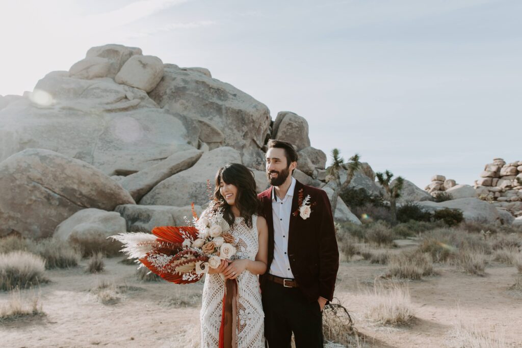 A woman holding her bouquet as her partner stands next to her during their sunrise Joshua Tree National Park elopement